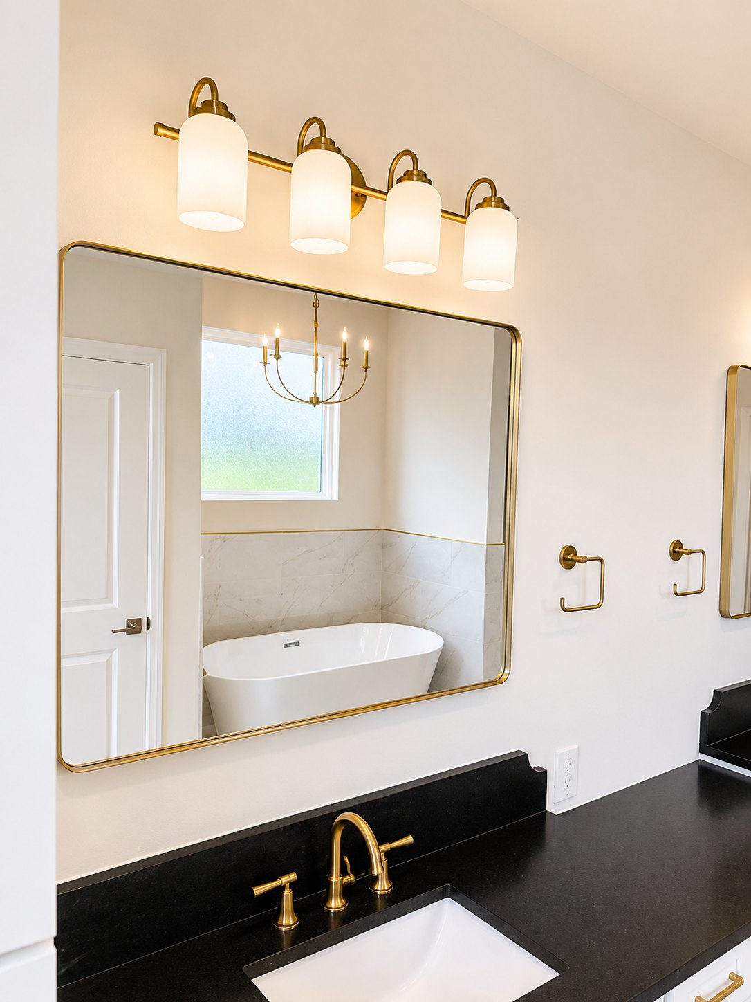 Primary bath vanity with black quartz counter, brass mirror, and tub reflection