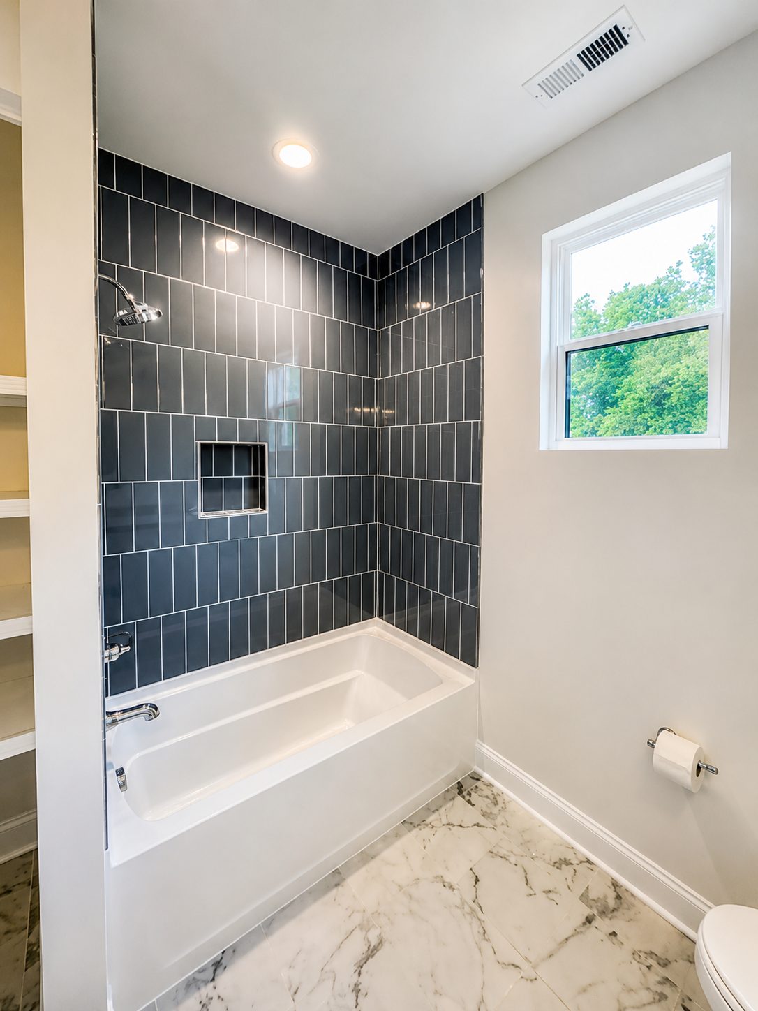 Guest bath with vertical navy tile surround and marble flooring