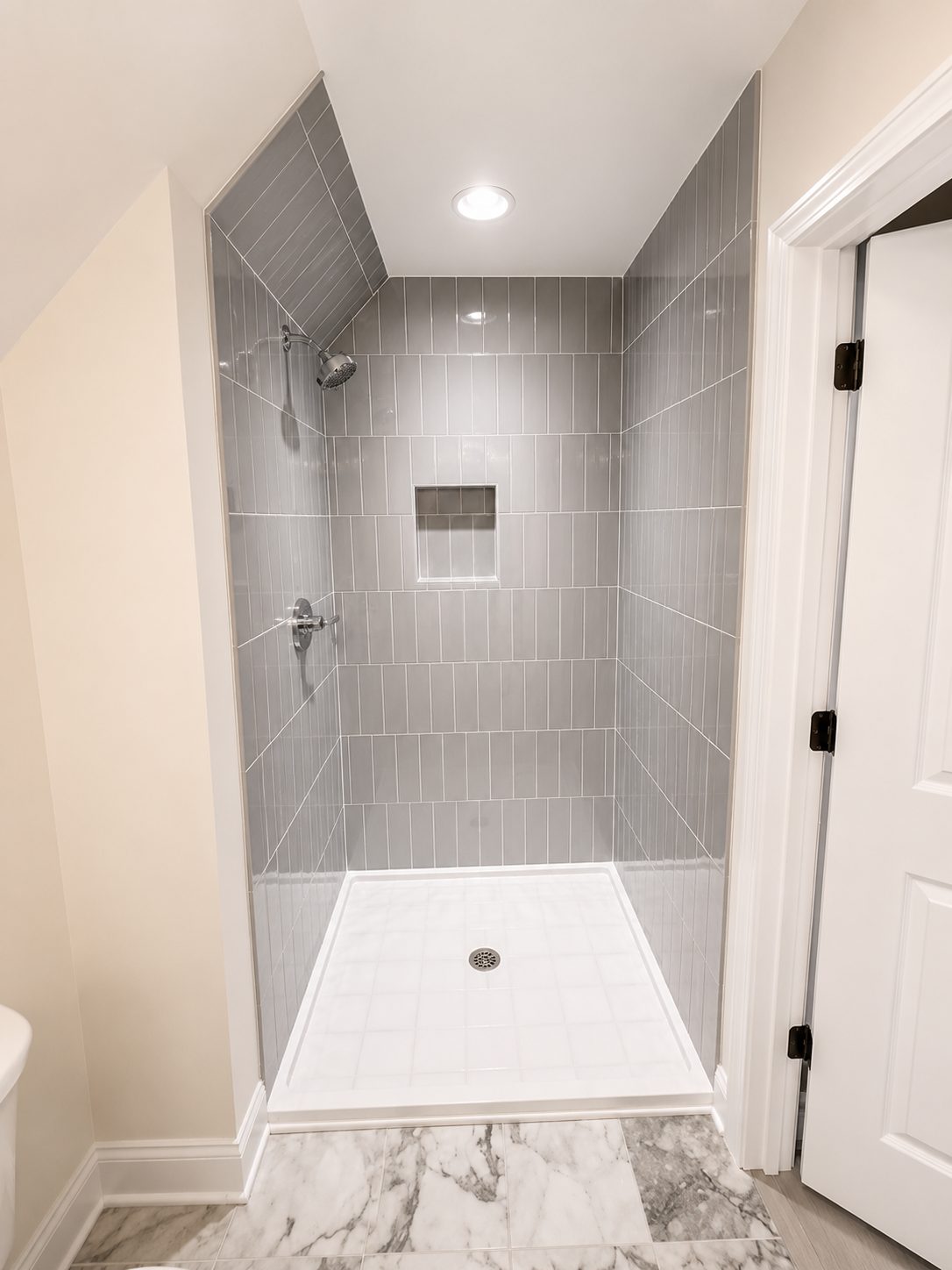 Tiled walk-in shower with vertical grey tile and marble flooring