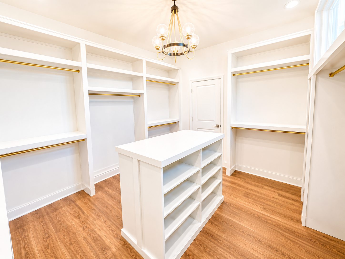 Primary walk-in closet with custom white built-ins, brass rods, and center island