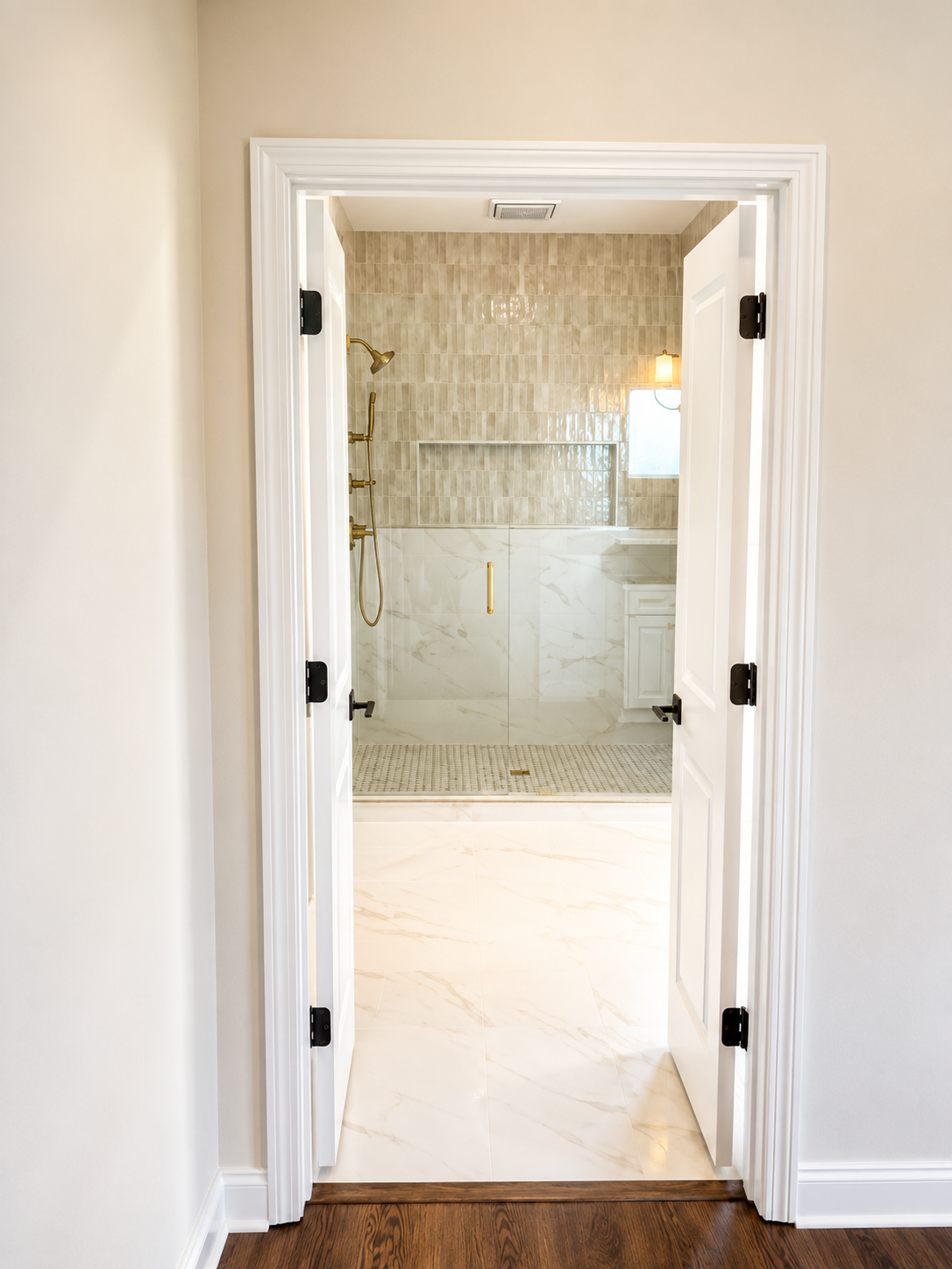 Double doors opening to the primary bath with glass shower and marble flooring